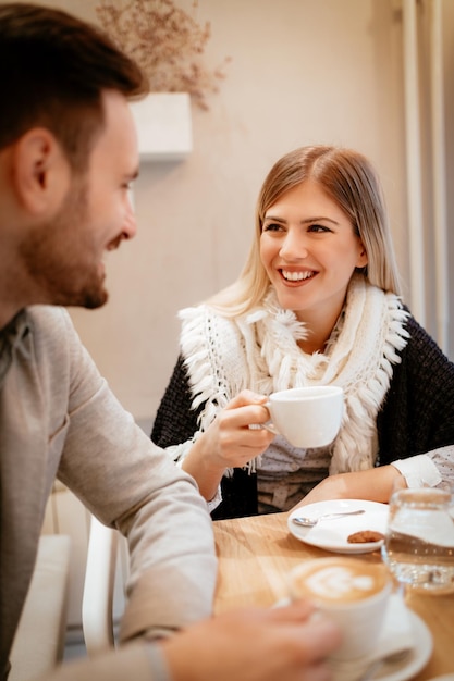 커피를 마시고 카페에서 그녀의 남자 친구와 이야기 하는 젊은 웃는 여자.