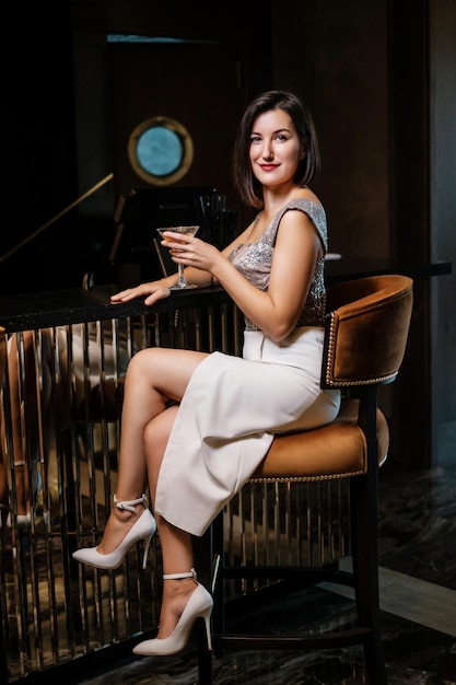 Young smiling woman in evening dress drinking at bar