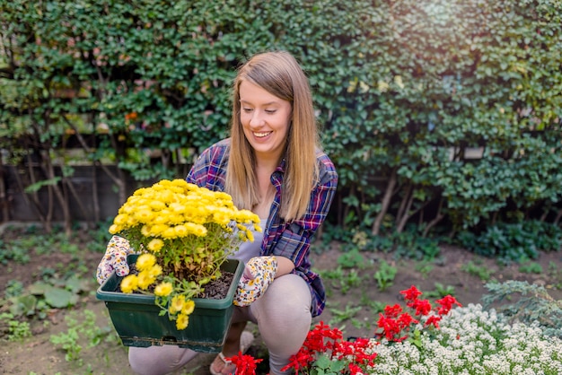 Young smiling woman florist working in the garden. Portrait of smiling young woman holding pot with beautiful flowers in a garden