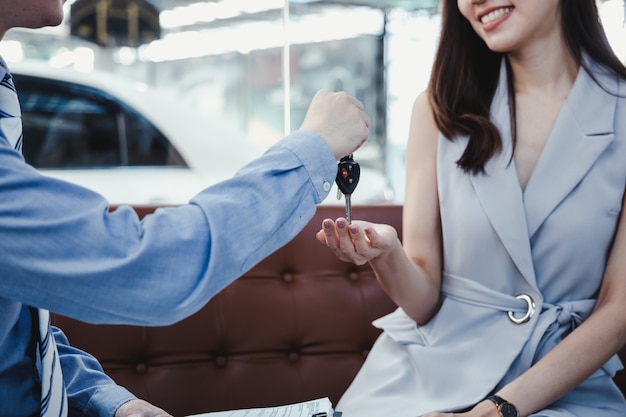 新しい車のキーを得る若い笑顔の女性。