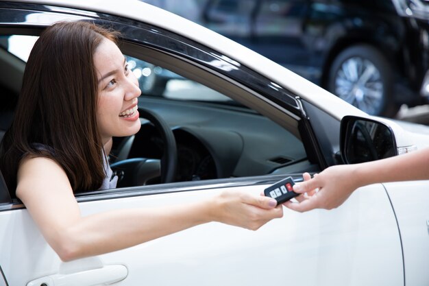 新しい車のキーを得る若い笑顔の女性。