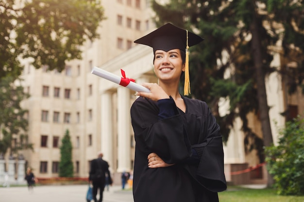 卒業証書、コピースペースを保持している大学で彼女の卒業式の日に若い笑顔の女性。教育、資格およびガウンの概念。