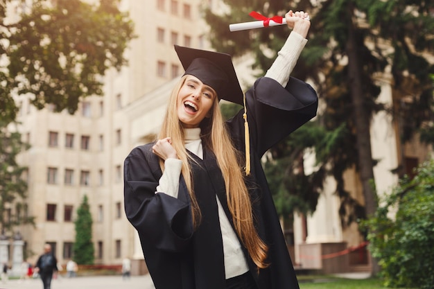 卒業証書、コピースペースを保持している大学で彼女の卒業式の日に若い笑顔の女性。教育、資格およびガウンの概念。