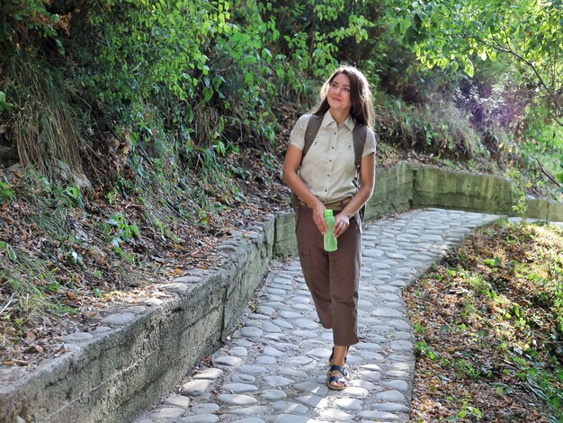 Young smiling woman hiking with bottle in his hands leisurely goes on rocky path