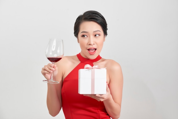 Young smiling woman hold christmas gift box. Isolated portrait of a beautiful girl with wine glass on studio background.