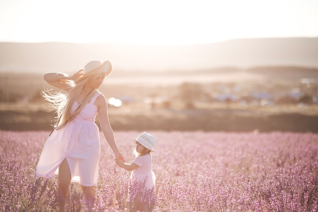 ラベンダーの牧草地を歩く女の赤ちゃんを保持している若い笑顔の女性