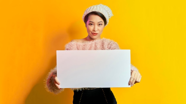 Young smiling woman holding a blank sheet of paper for advertising