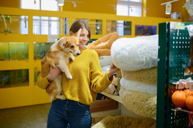 Foto giovane donna sorridente con un cane corgi in mano che sceglie un posto morbido dove dormire al negozio di animali domestici