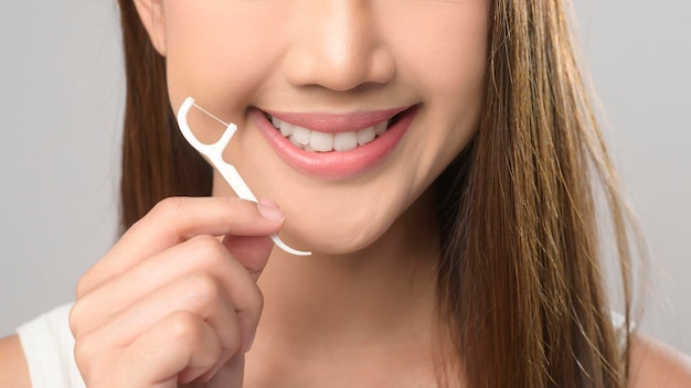 ホワイト バック グラウンド スタジオ歯科にデンタルフロスを保持している若い笑顔の女性