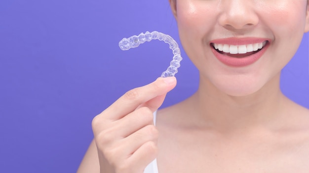 Молодая улыбающаяся женщина, держащая брекеты invisalign в студии, стоматологическом здравоохранении и ортодонтической концепции.