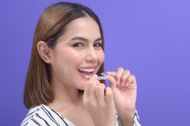 A young smiling woman holding invisalign braces in studio, dental healthcare and Orthodontic concept.