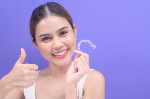 Молодая улыбающаяся женщина, держащая брекеты invisalign в студии, стоматологическом здравоохранении и ортодонтической концепции.