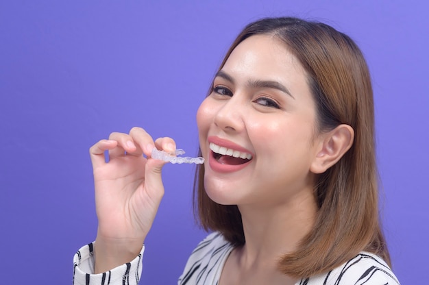 A young smiling woman holding invisalign braces in studio, dental healthcare and Orthodontic concept.