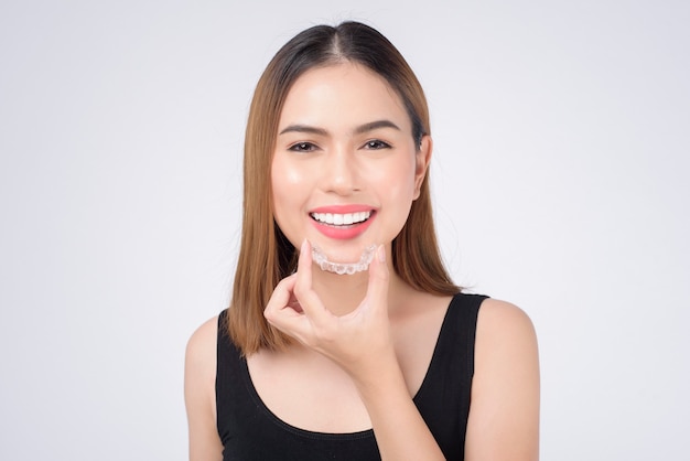 Young smiling woman holding invisalign braces in studio, dental healthcare and Orthodontic concept