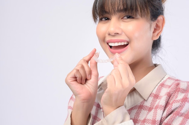 A young smiling woman holding invisalign braces over white background studio