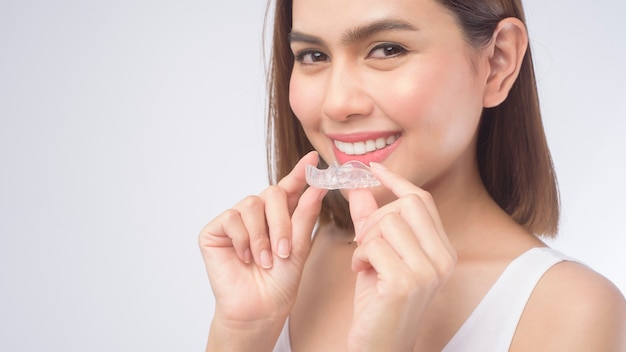 Молодая улыбающаяся женщина, держащая брекеты invisalign на белом, стоматологическом здравоохранении и ортодонтической концепции.