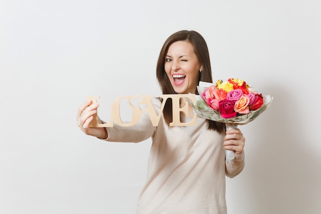 Young smiling woman holding wooden word Love, bouquet of beautiful roses flowers isolated on white background. Copy space for advertisement. St. Valentine's Day or International Women's Day concept.
