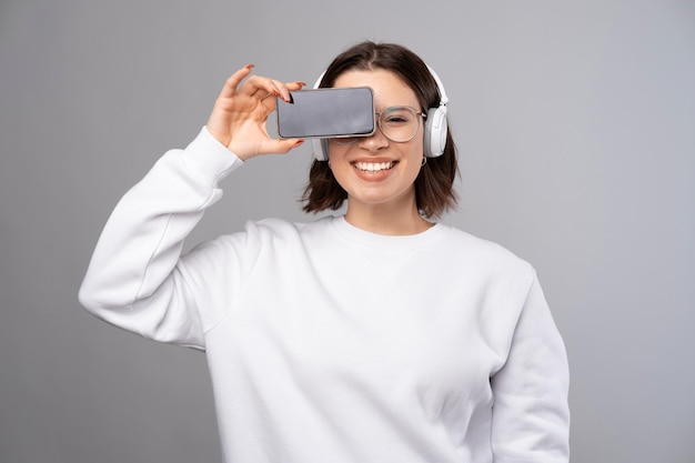 Young smiling woman is covering one eye with a phone Copy space on screen