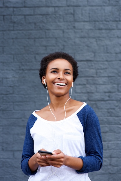 イヤホンと携帯電話で音楽を聴く若い笑顔の女性