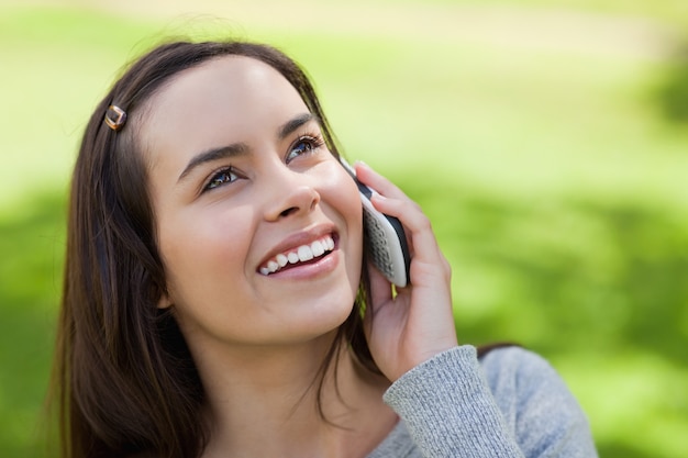 Молодая женщина улыбается глядя во время разговора по телефону