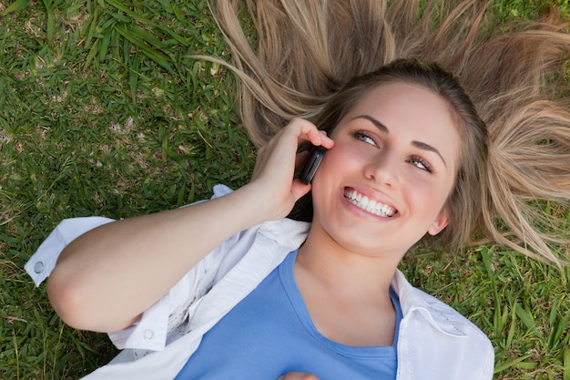 Young smiling woman lying on her back while using her cellphone