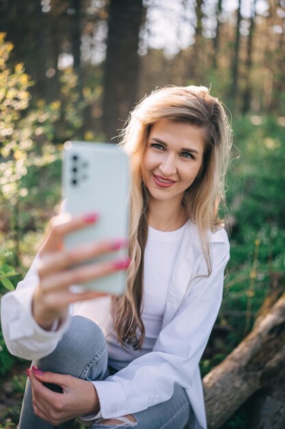 森で携帯電話を使ってセルフィーを撮る若い笑顔の女性