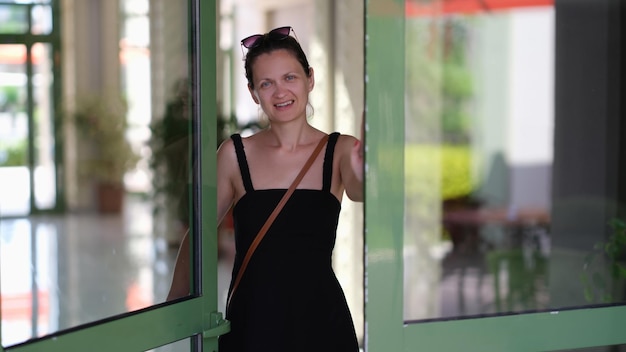 Young smiling woman opens a glass door