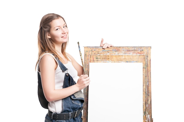 Foto giovane pittore sorridente della donna con il pennello in piedi al cavalletto