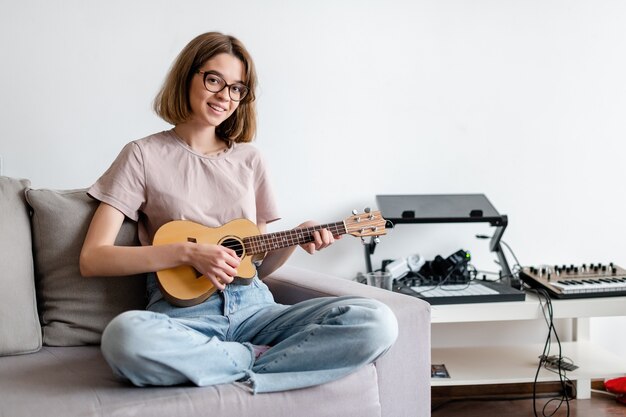 Giovane donna sorridente che gioca ukulele a casa