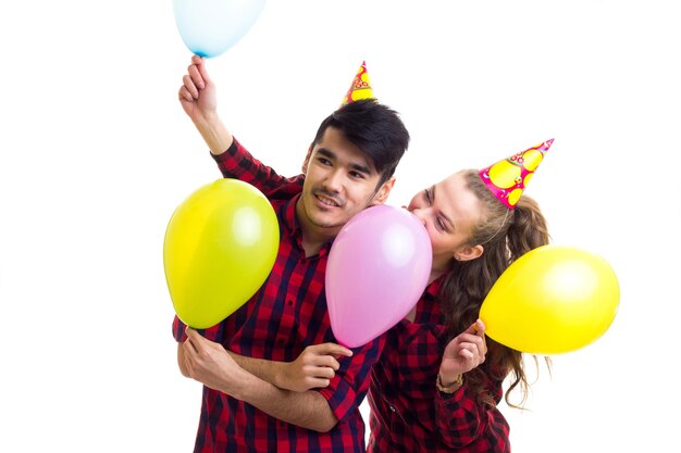 Young smiling woman and pleasant man in red plaid shirts with celebrating hats blowing balloons