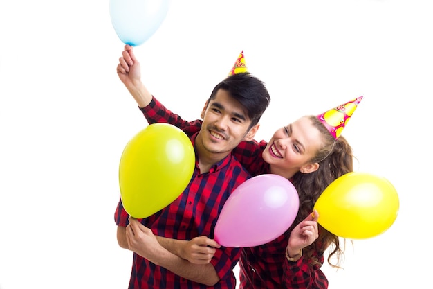 Young smiling woman and pleasant man in red plaid shirts with celebrating hats blowing balloons