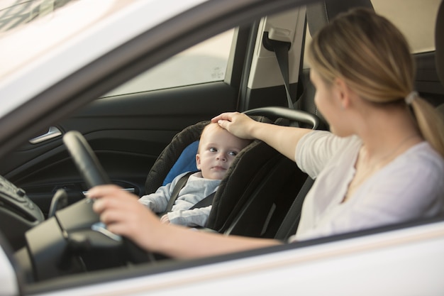 Young smiling woman posing in car with her baby boy