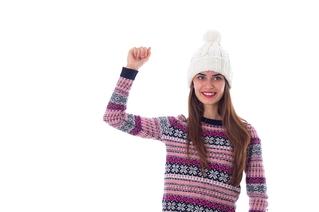 Young smiling woman in purple sweater and white hat showing fist on white background in studio