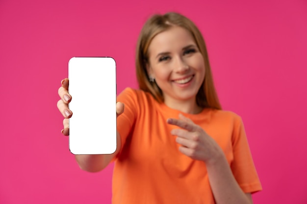 Young smiling woman showing blank screen smartphone in studio