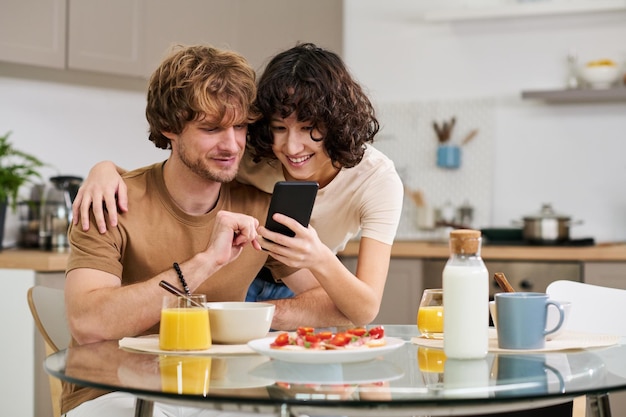 Young smiling woman showing something in smartphone to her husband