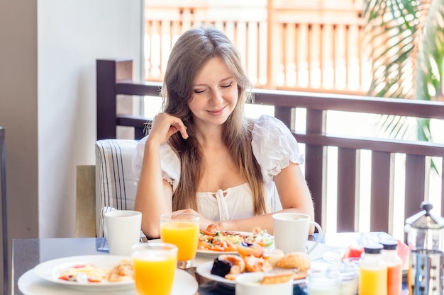 食べ物でいっぱいの皿と朝食に座っている若い笑顔の女性