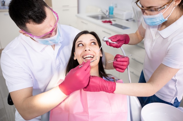 Giovane donna sorridente seduta sulla poltrona del dentista con due medici che lavorano