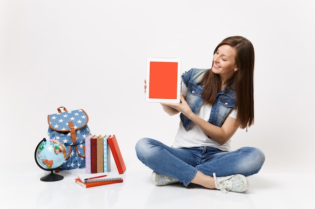 Young smiling woman student looking on tablet pc computer with blank black empty screen sit near globe backpack, school books isolated