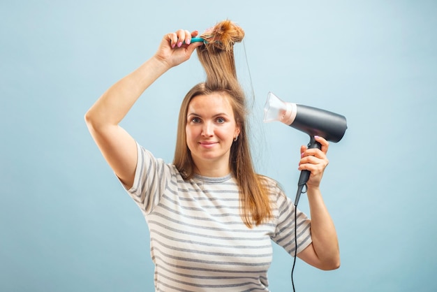 Young smiling woman using hair dryer on blue background hair care concept