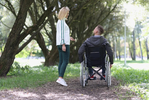 若い笑顔の女性は車椅子の友情と人々のサポートで男性と一緒に公園を歩く