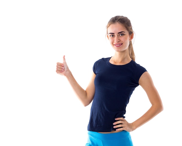 Young smiling woman wearing in blue T-shirt and leggings showing thumb up on white background in studio