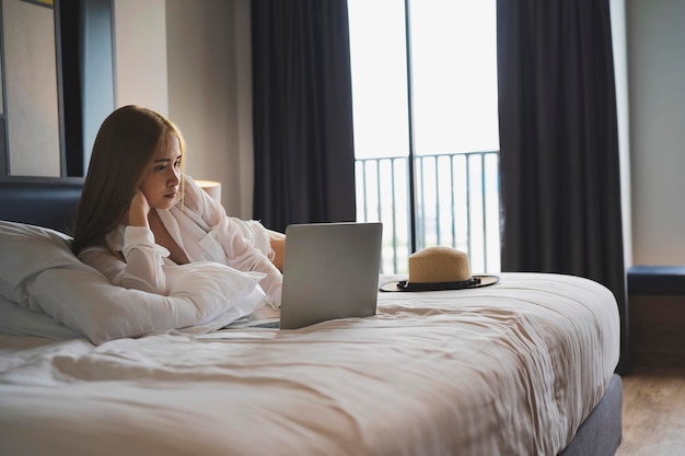 Young smiling woman wearing a dressing gown thinking about a future travel listening to a favorite musical track via laptop