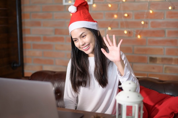 A young smiling woman wearing red santa claus hat making video\
call on social network with family and friends on christmas\
day.