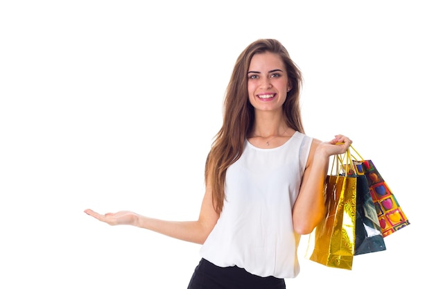 Young smiling woman in white blouse and black skirt holding shopping bags and pointing down