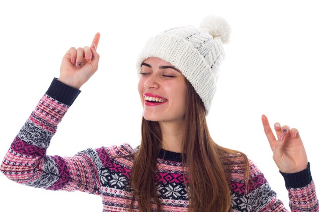 Young smiling woman in white hat and purple sweater holding hands up on white background in studio