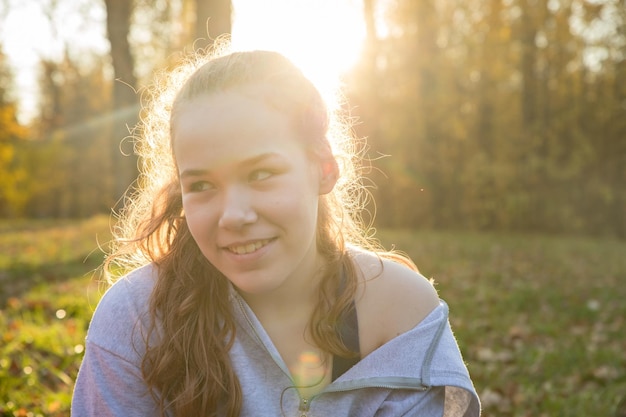 秋の公園に座っている白いパーカーの若い笑顔の女性