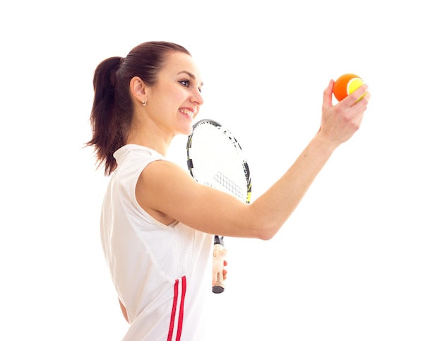 Young smiling woman in white sports shirt with brown ponytail holding tennis raquet and yellow ball