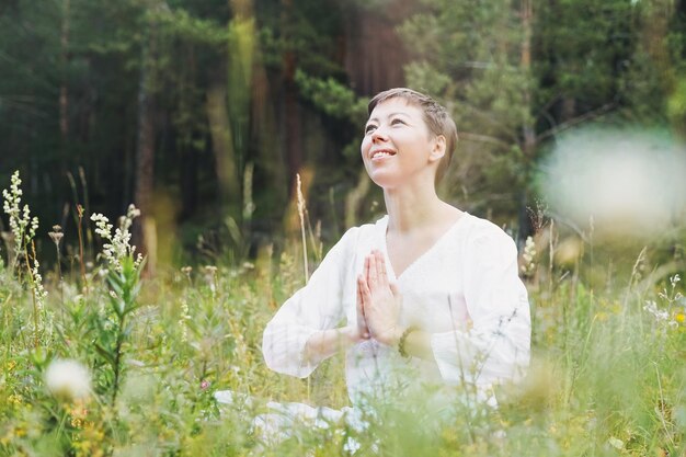 Young smiling woman with beads practice yoga outdoors in the forest New normal social distance Physical and mental health