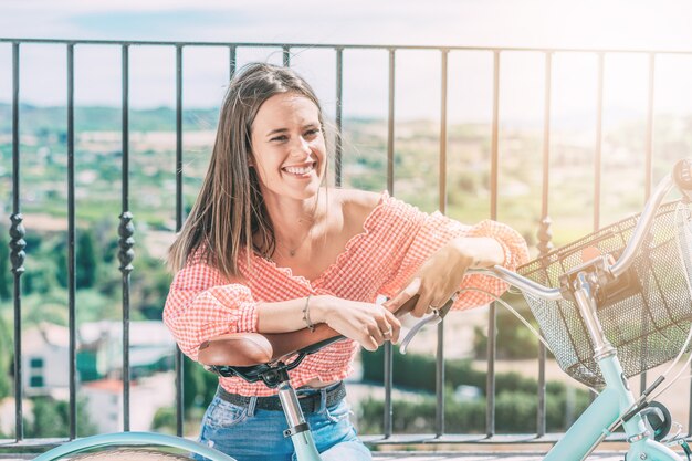 Giovane donna sorridente con la bicicletta riposa seduta con un bellissimo paesaggio