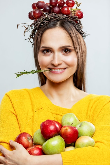 Giovane donna sorridente con frutta. una bella bruna in un maglione giallo con uva viola in testa